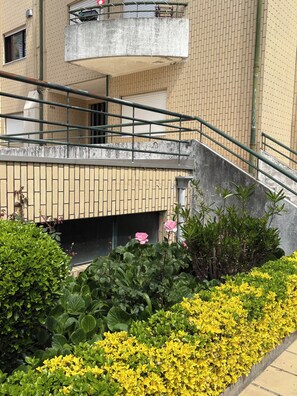 A multi-story building with a staircase, a balcony, and a garden area with yellow flowers.