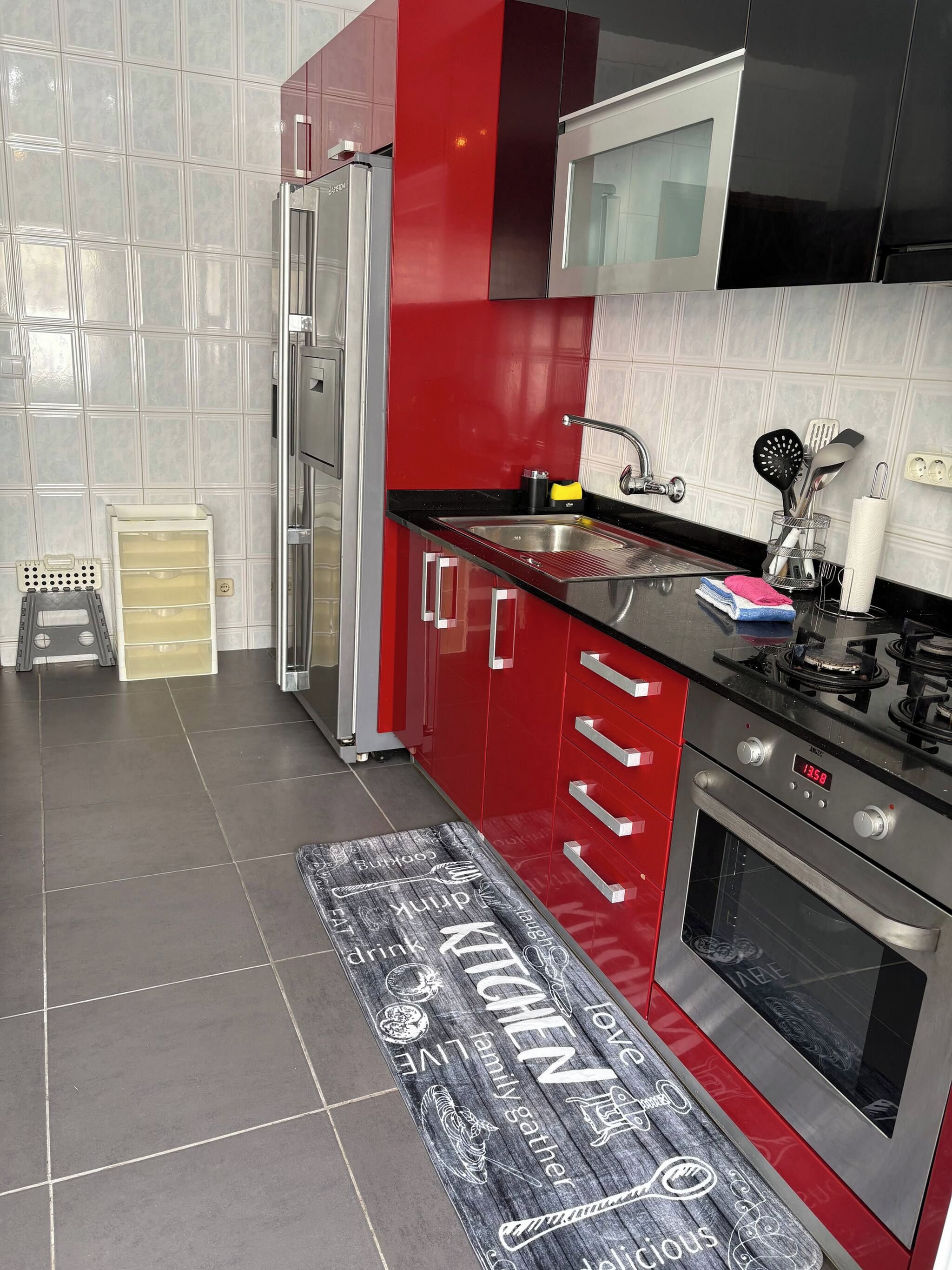 Una cocina moderna con electrodomésticos de acero inoxidable, armarios rojos y una encimera negra.