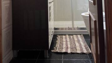 Une salle de bain dotée d’une douche à parois de verre, d’un meuble-lavabo en bois foncé et d’un tapis à motifs sur le sol.