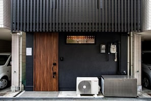 A building entrance with a dark facade, a wooden door, and an air conditioning unit. - NIKYO Hoshi House Private Villa OSAKA (Osaka)