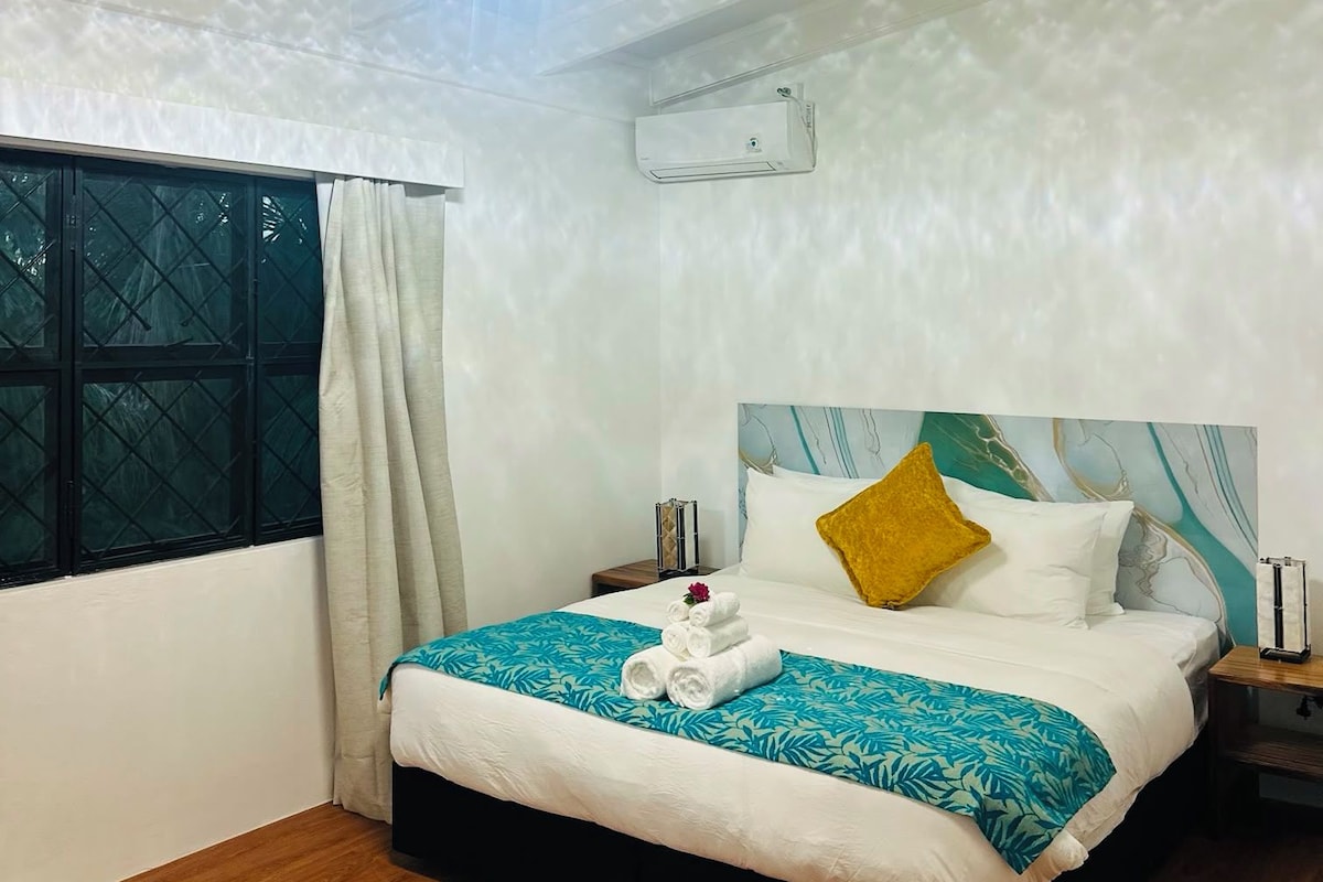 A hotel room with a bed, a window with curtains, a ceiling light, and a wall-mounted air conditioner.