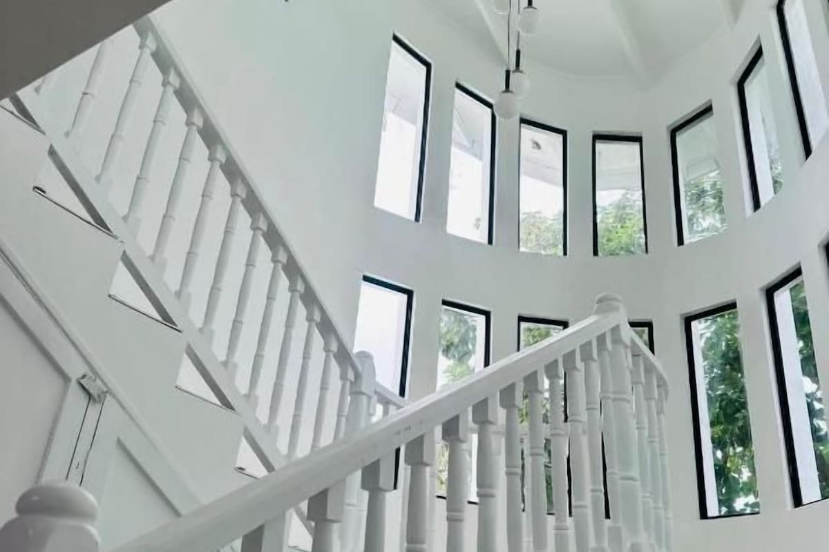 A white staircase with a modern design, leading to a high ceiling with large windows.