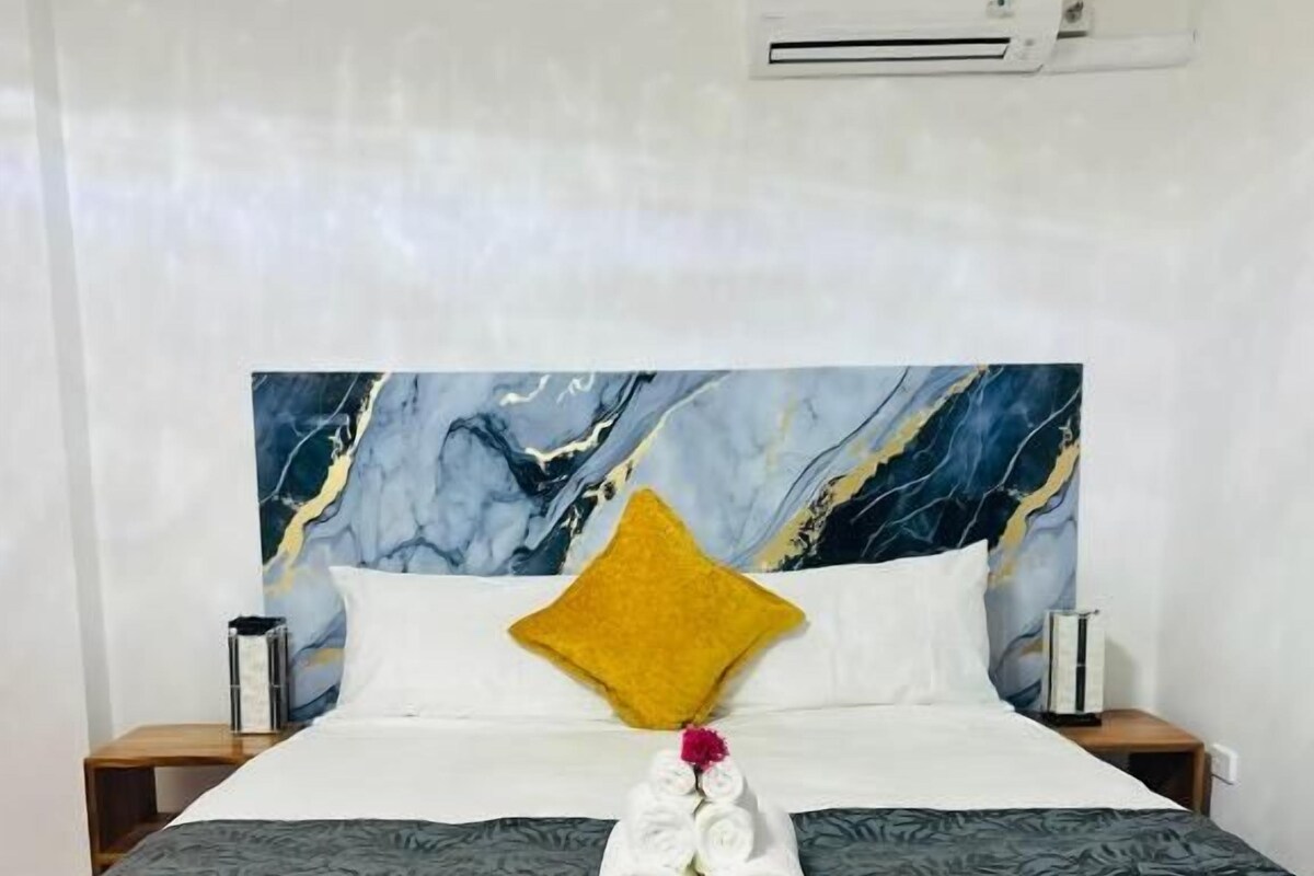 A hotel room with a bed, a nightstand, an air conditioning unit, and a marble-patterned headboard.