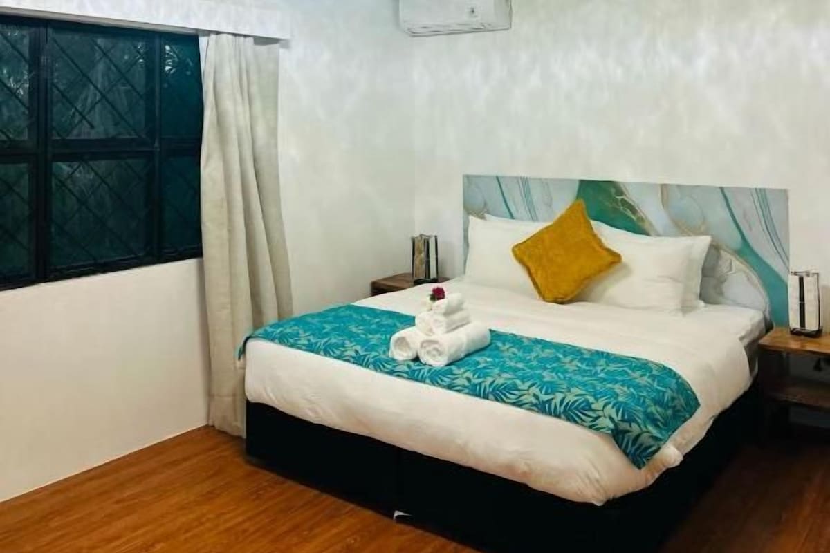 A hotel room with a bed, a bedside table, a window with curtains, and a ceiling light.