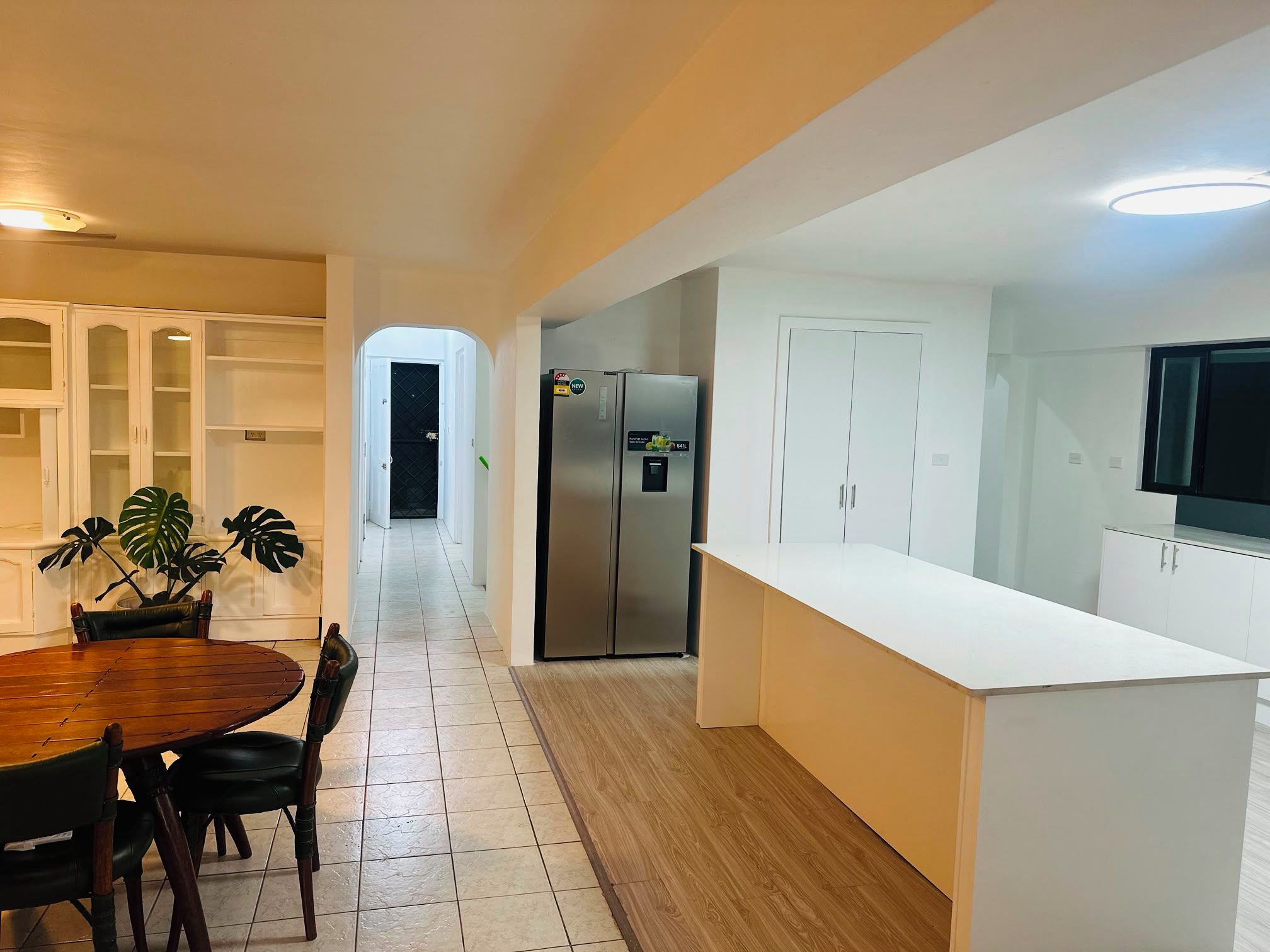 A modern kitchen with white cabinetry, a stainless steel refrigerator, and a dining area with a wooden table and chairs.
