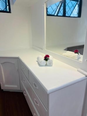A white dresser with a mirror, two rolled towels, and a red flower. - Residence No. 5 (Martintar, Nadi)