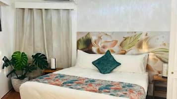 Een slaapkamer met een bed, een plafondventilator, een airconditioningapparaat, een raam met gordijnen en een kamerplant.