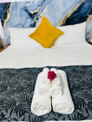 A neatly made bed with a white pillow and a yellow accent pillow, a folded white towel with a red flower on top, and a patterned pillowcase. - Residence No. 5 (Martintar, Nadi)