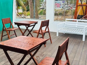 An outdoor seating area with wooden tables and chairs, a white bench, and a view through a chain-link fence. - Residence No. 5 (Martintar, Nadi)