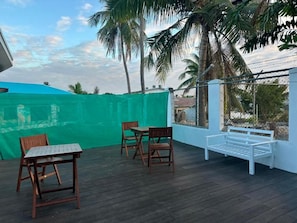 An outdoor patio with a wooden table and chairs, a white bench, and a green fence.