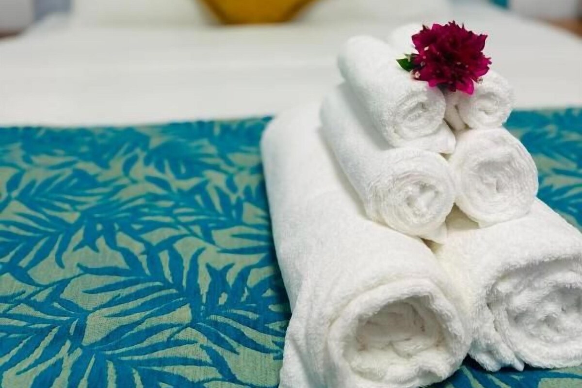 A neatly made bed with rolled white towels and a decorative flower on top, set against a patterned blue and white bedspread.