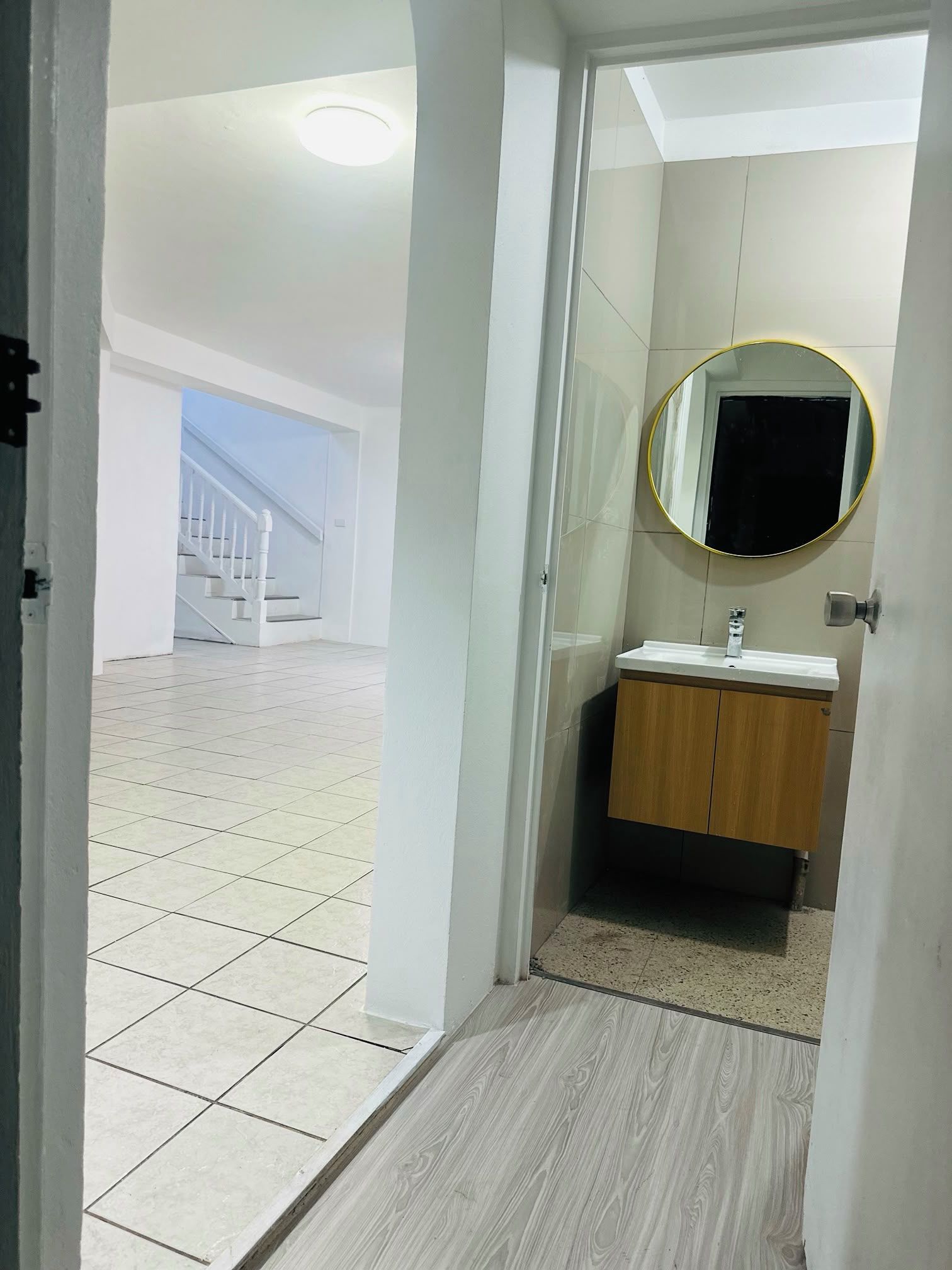 A bathroom with a wooden vanity, a round mirror, and a tiled floor.