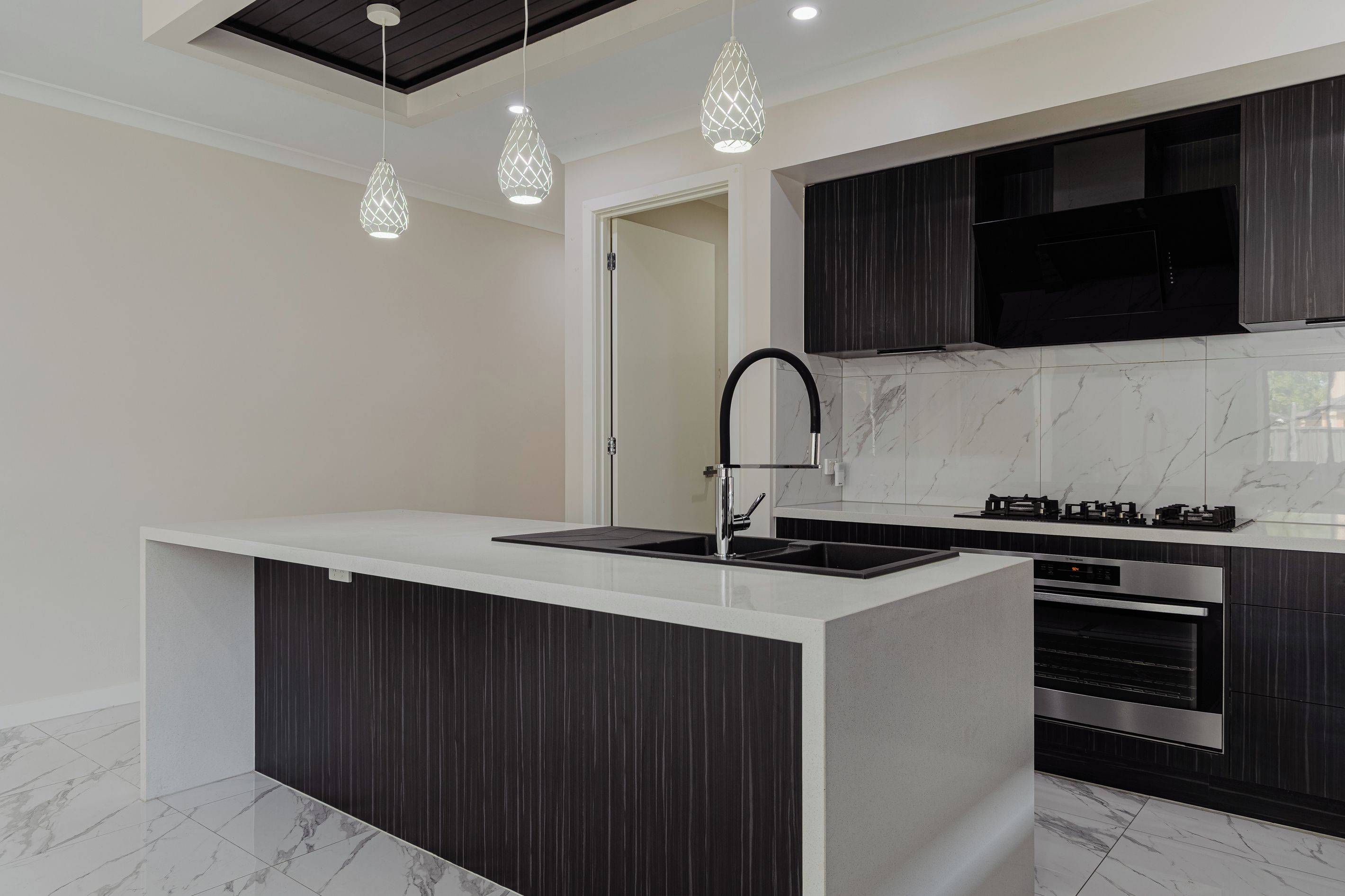 A modern kitchen with a central island, black cabinetry, a stainless steel sink, and a gas stove.