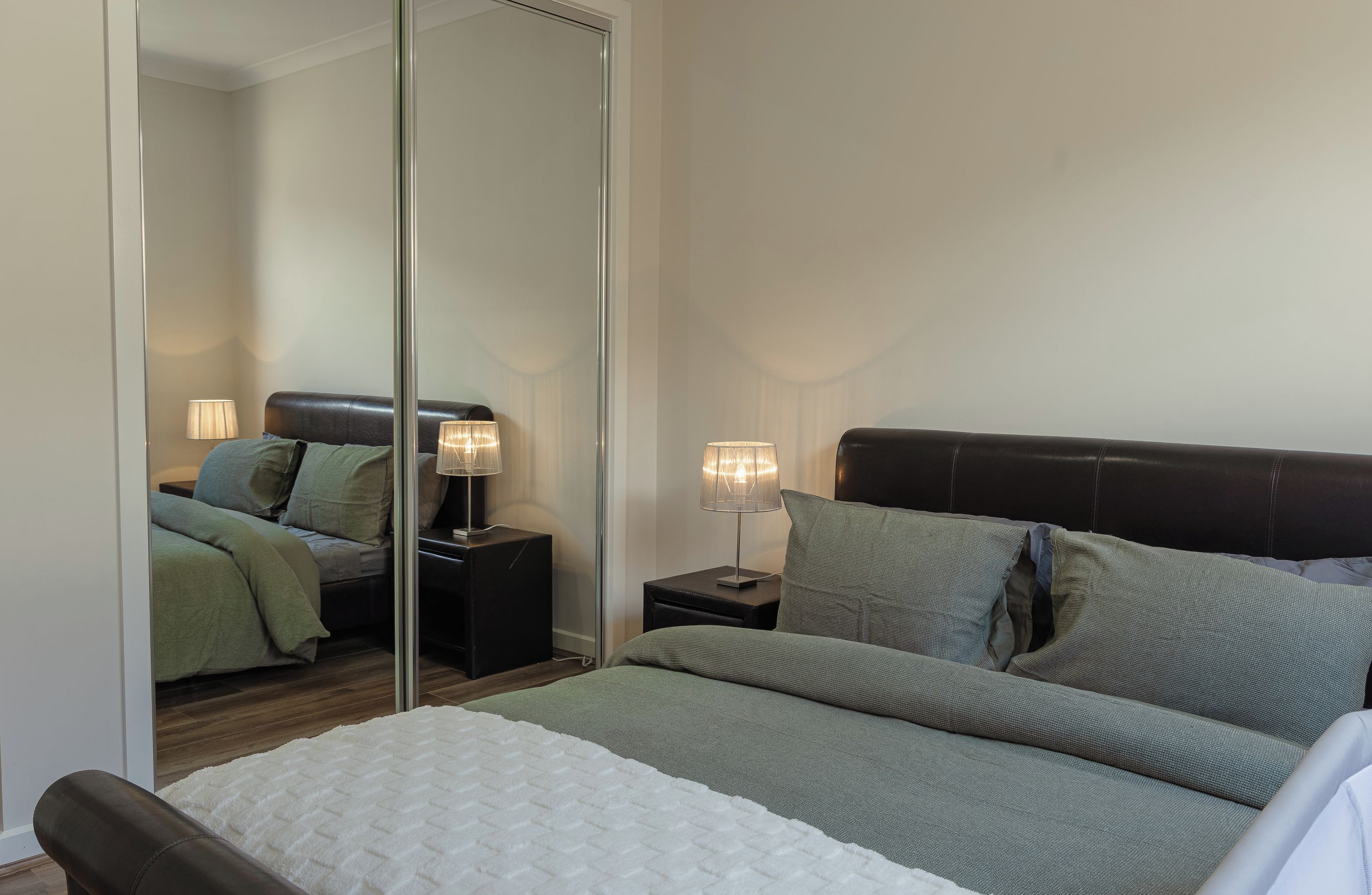 A bedroom with a bed, two bedside tables, a mirror, and a nightstand.
