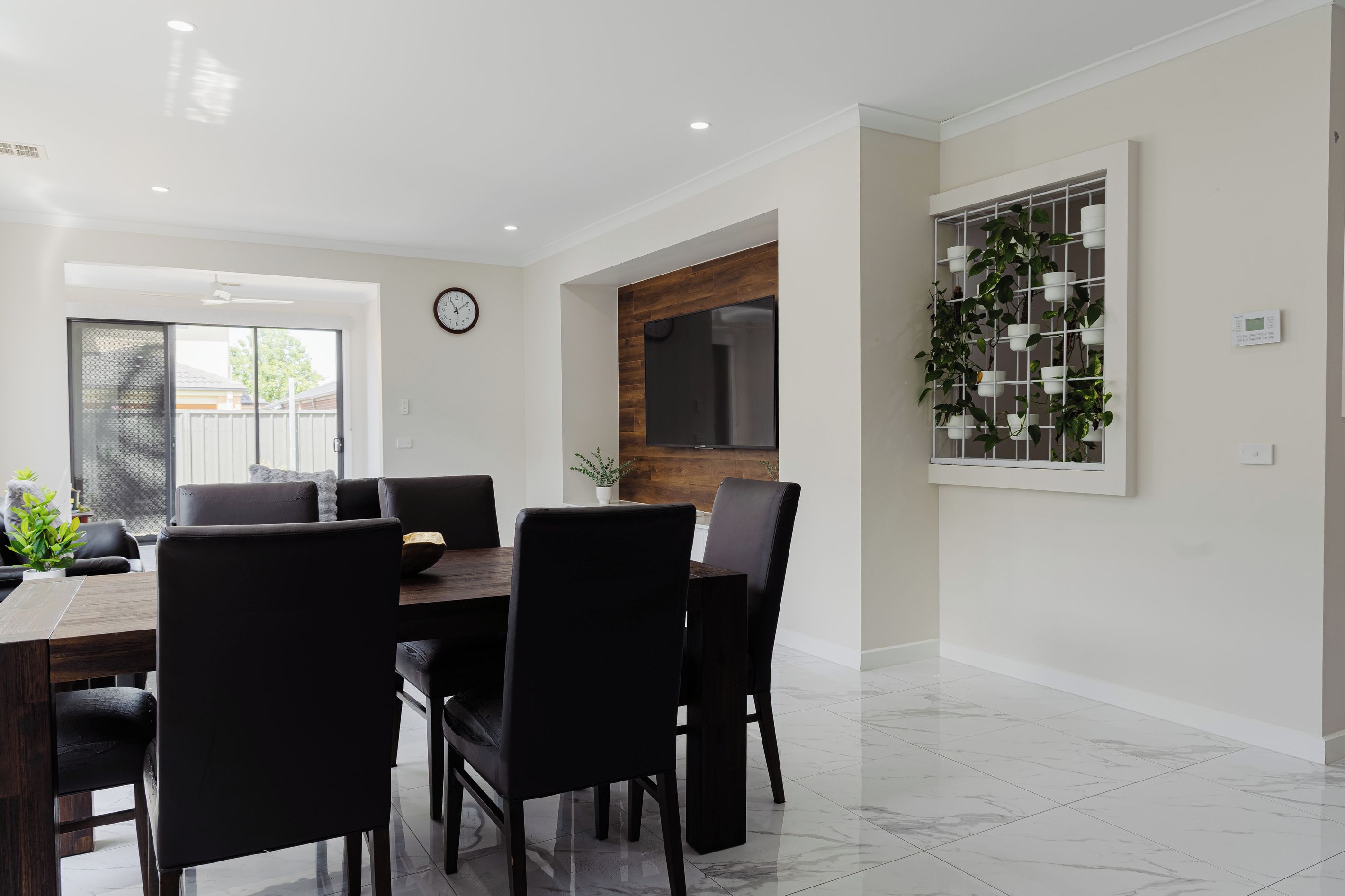 A modern dining area with a wooden table, black chairs, and a potted plant.