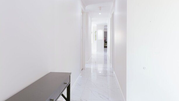 Un pasillo con paredes blancas y piso de mármol que conduce a una habitación con una cama.