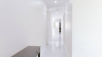 A hallway with white walls and a marble floor, leading to a room with a bed.