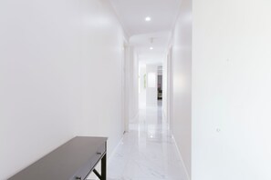 Passadís amb parets blanques i un terra de marbre, que condueix a una habitació amb un llit.