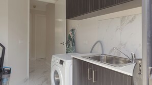 Cocina compacta con lavadora integrada, un lavabo y una puerta que da a otra habitación.