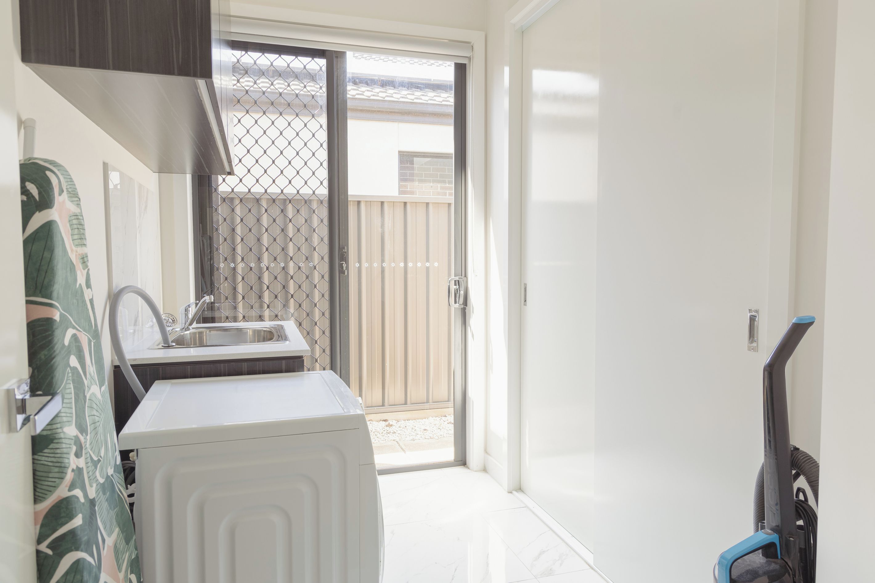 Cocina compacta con lavamanos, lavadora blanca y puerta corrediza de vidrio que da a un área exterior.