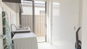 Cocina compacta con lavamanos, lavadora blanca y puerta corrediza de vidrio que da a un área exterior.