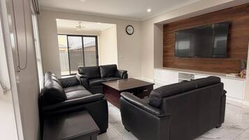 A modern living room with a sectional sofa, a coffee table, and a flat-screen TV mounted on the wall.