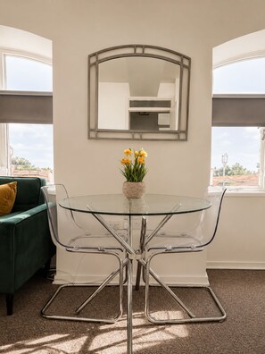 A room with a glass table surrounded by metal chairs, a mirror on the wall, and a window with a view. - Comfortable Apartment with free parking sleeps 4 and is close to Longleat. (Westbury)