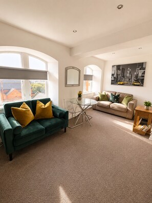 A modern living room with a green sofa, a beige sofa, and a glass coffee table. - Comfortable Apartment with free parking sleeps 4 and is close to Longleat. (Westbury)