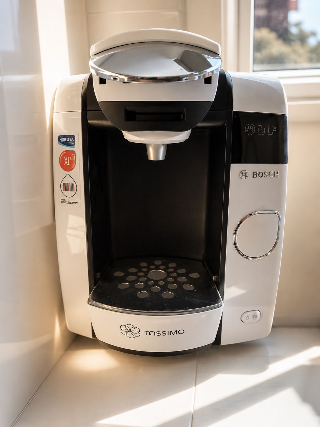 Une machine à café Tassimo au design noir et blanc, posée sur un rebord de fenêtre.