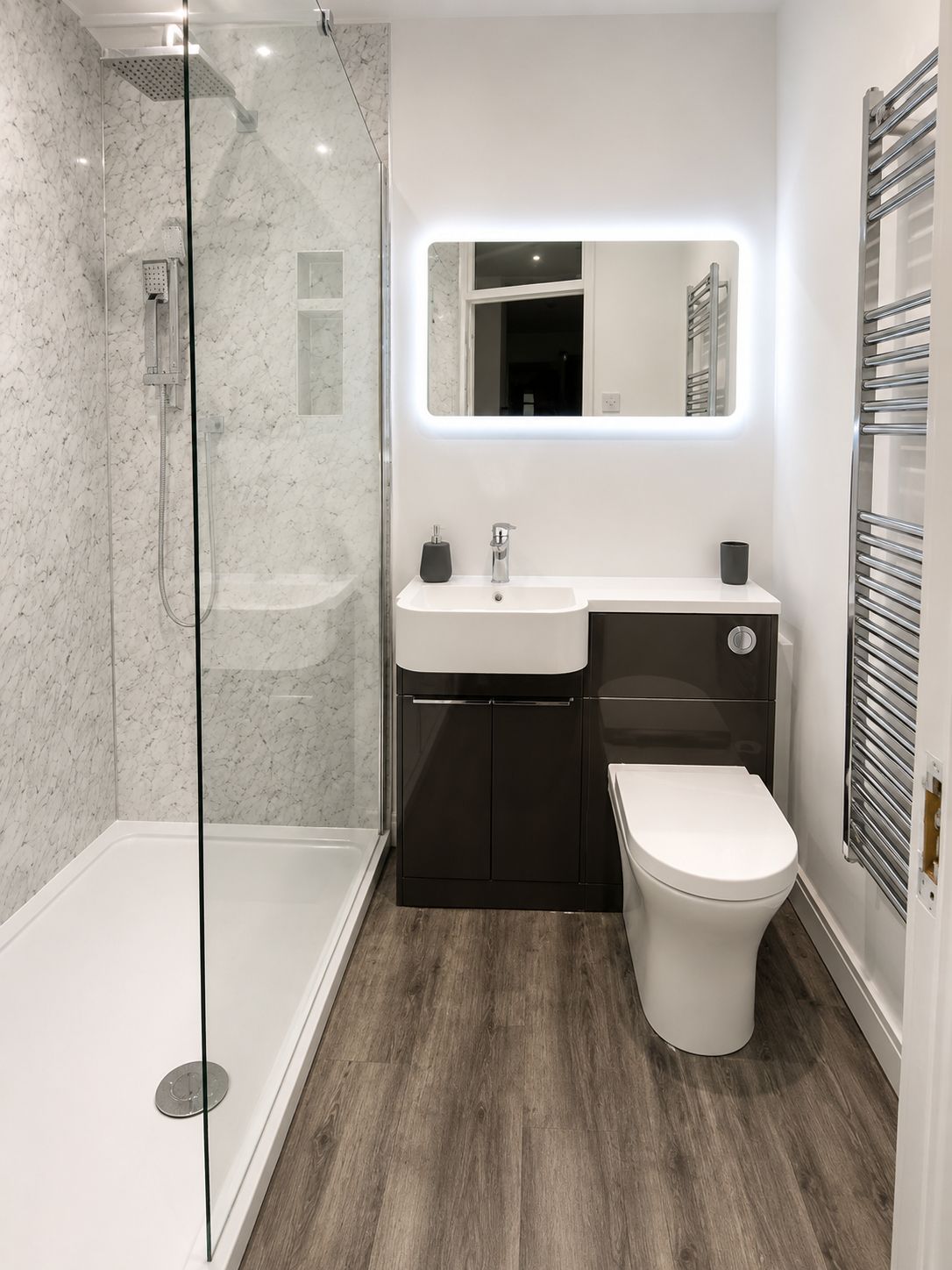 Un baño moderno con ducha envuelta en vidrio, un lavabo blanco, un mueble oscuro y un inodoro blanco.
