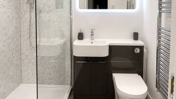 Un baño moderno con ducha envuelta en vidrio, un lavabo blanco, un mueble oscuro y un inodoro blanco.
