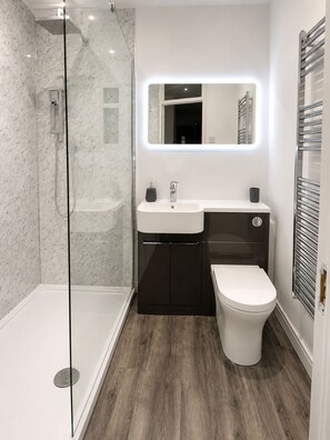 A modern bathroom with a glass-enclosed shower, a white sink, a dark cabinet, and a white toilet. - Comfortable Apartment with free parking sleeps 4 and is close to Longleat. (Westbury)