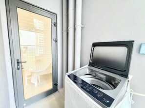 Ein Waschraum mit einer Waschmaschine, einer Tür und Blick auf einen Balkon mit Tisch und Stühlen.