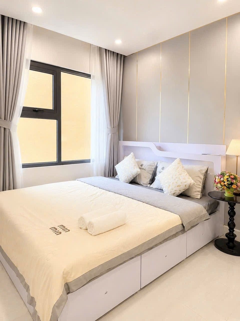 Un dormitorio moderno con una cama grande, una mesita de noche con lámpara y una ventana con cortinas.