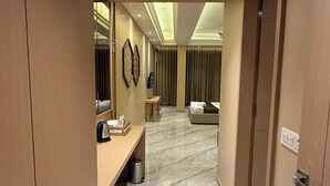 A hotel hallway with a marble floor, a reception desk, a bed, and a bathroom visible in the background. - Hotel Tejasvi Inn (Junagadh)