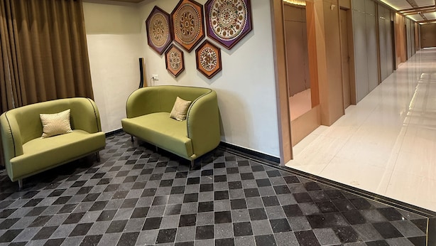 A hotel lobby with a checkered floor, two green sofas, a wall with decorative patterns, and a corridor leading to rooms. - Hotel Tejasvi Inn (Junagadh)