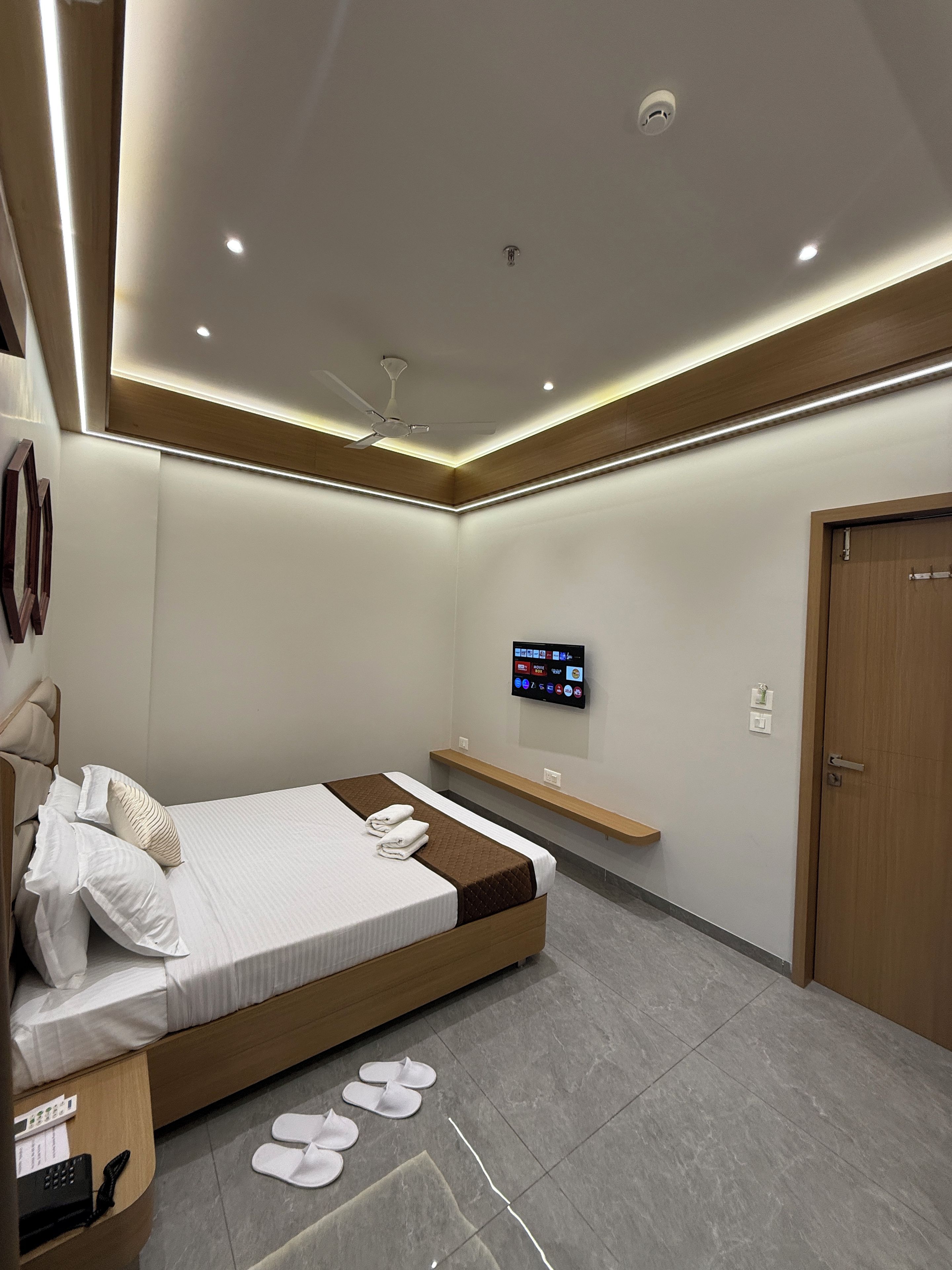 A modern hotel room with a bed, a TV mounted on the wall, and a wooden door.