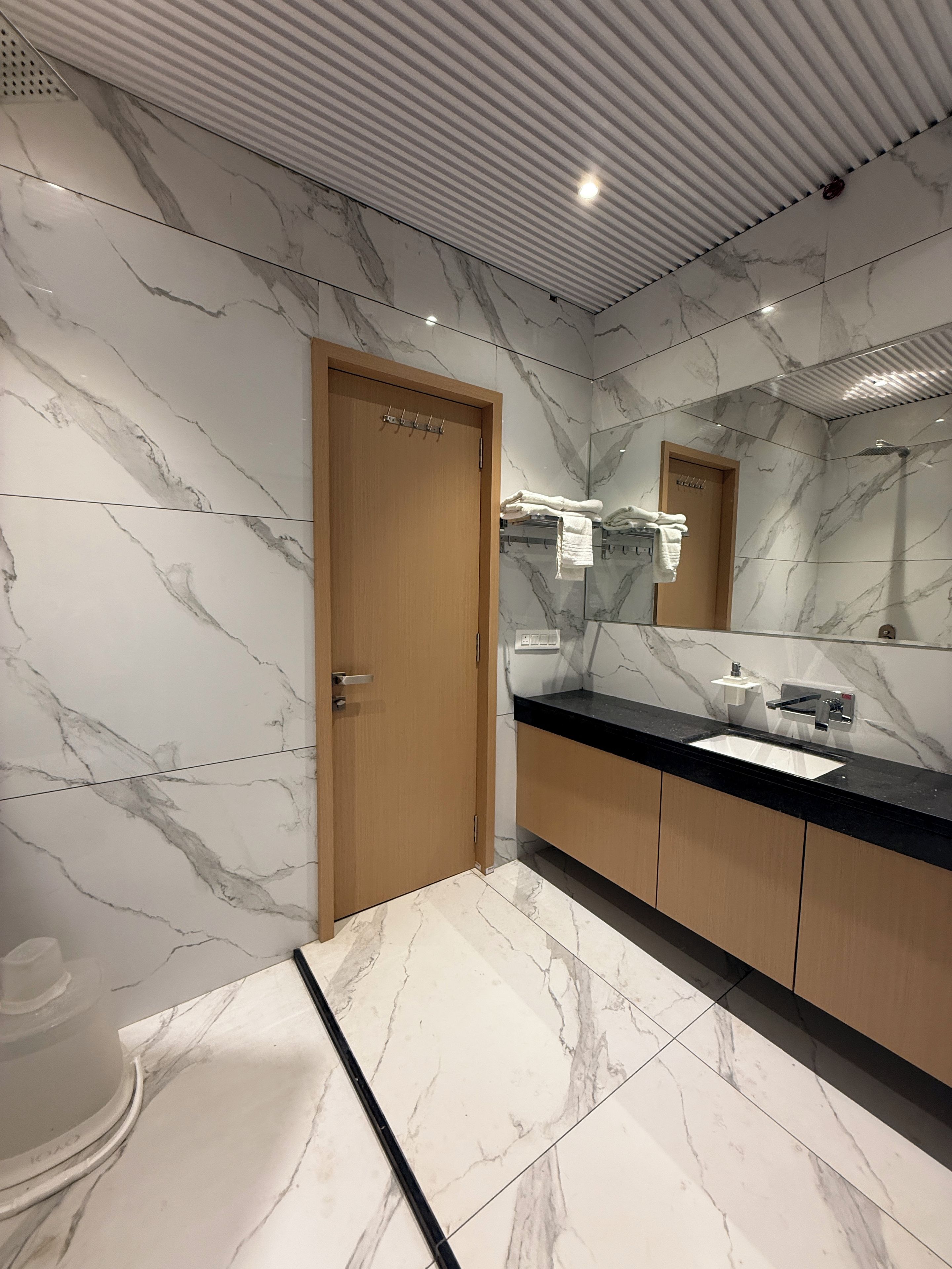 A modern bathroom with marble walls, a wooden door, a black countertop, and a mirror.