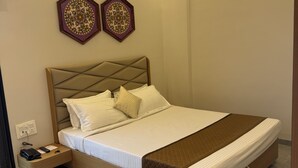 A modern bedroom with a large bed, bedside tables, and decorative wall art. - Hotel Tejasvi Inn (Junagadh)