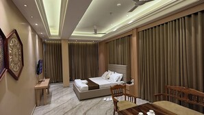 A modern hotel room with a bed, a dining table, and a ceiling fan. - Hotel Tejasvi Inn (Junagadh)
