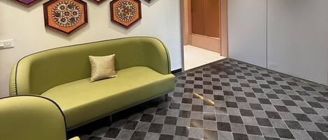 A lobby with a green sofa, patterned wall decorations, and a checkered floor.