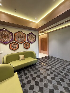 A lobby with a green sofa, patterned wall decorations, and a checkered floor. - Hotel Tejasvi Inn (Junagadh)
