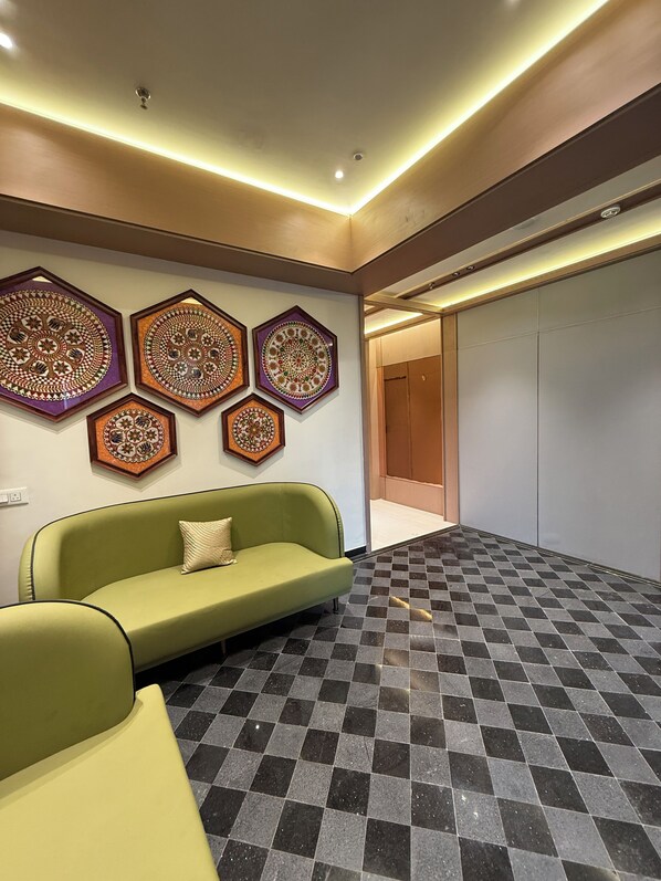 A lobby with a green sofa, patterned wall decorations, and a checkered floor.