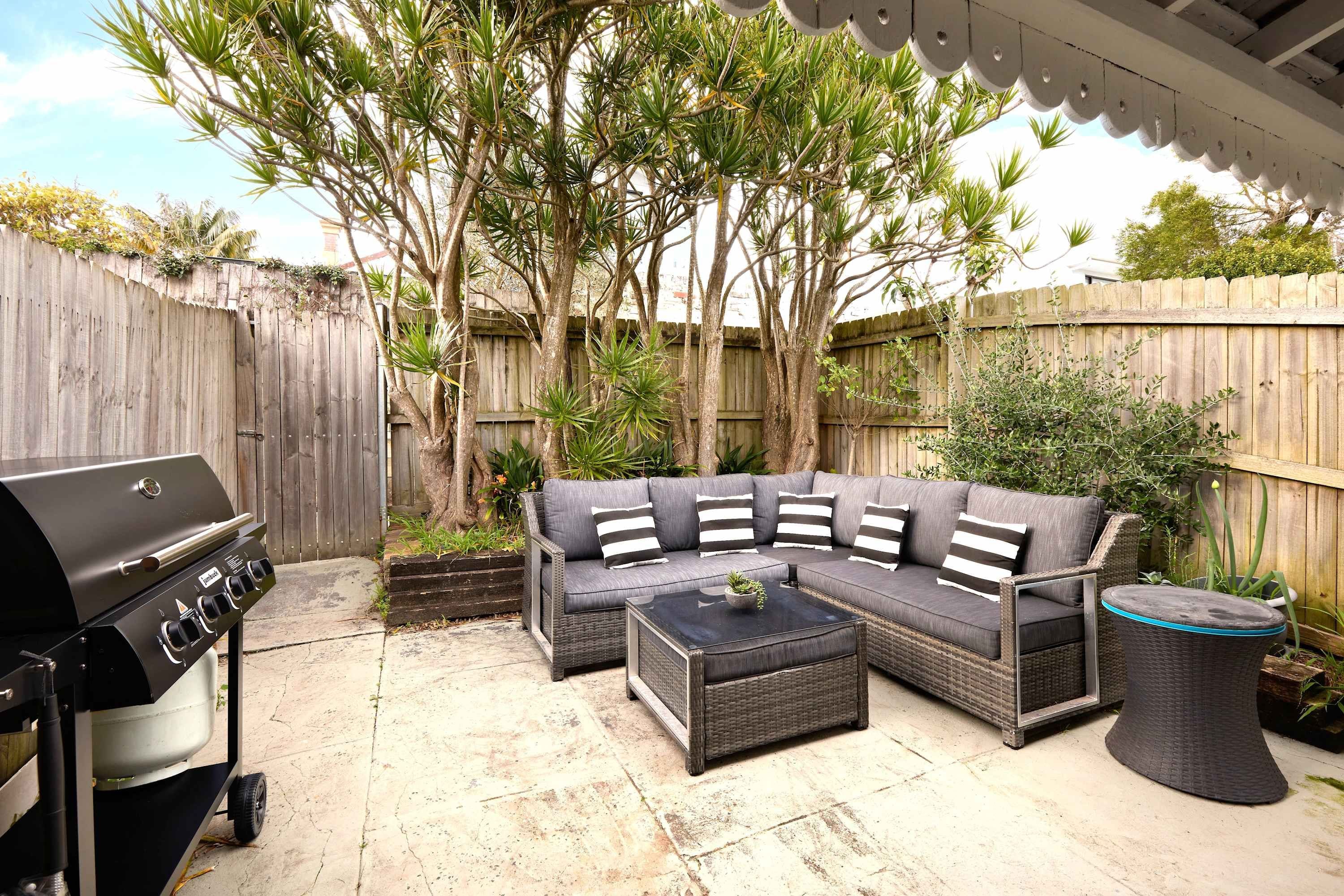 Une terrasse extérieure avec un canapé d’angle, une table basse ronde et un barbecue.