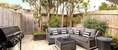 Un patio exterior con un sofá modular, una mesa redonda para café y una parrilla.