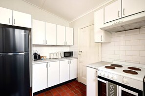 A kitchen with white cabinets, a black refrigerator, a microwave, a stove, and a tiled backsplash. - Sunny Bondi Junction 3BR | Backyard, BBQ & Bathtub (Bondi Junction)