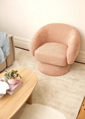 A round wooden table with a potted plant and books, a beige carpet, and a pink armchair with a wooden base. - Sunny Bondi Junction 3BR | Backyard, BBQ & Bathtub (Bondi Junction)