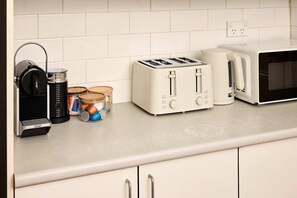 Une cuisine équipée d’une machine à café, d’un grille-pain et d’un four à micro-ondes, le tout posé sur un plan de travail.