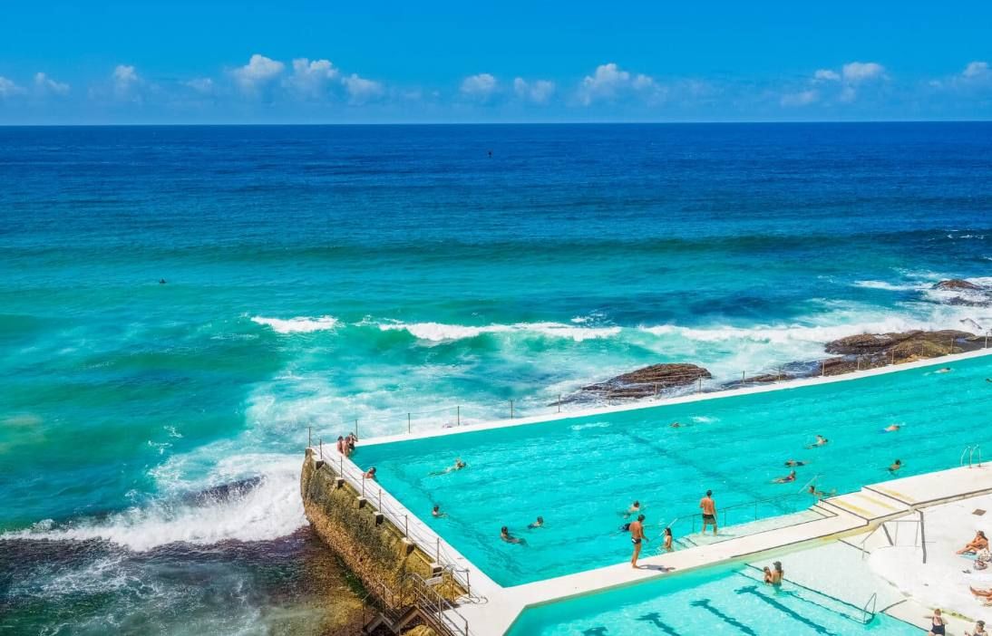 A clear view of a swimming pool adjacent to the ocean with waves crashing onto the shore.