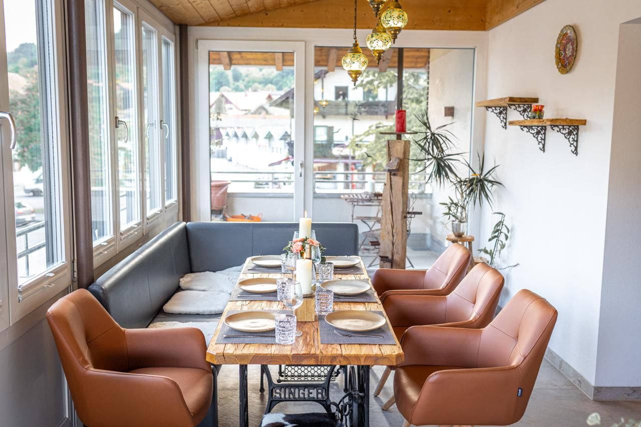 Un coin repas avec une table en bois dressée pour six personnes, entourée de fauteuils en cuir, et offrant une vue sur l’extérieur.